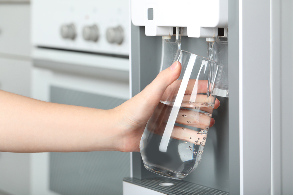 Woman filling glass with spring water cooler indoors, closeup. Refreshing drink